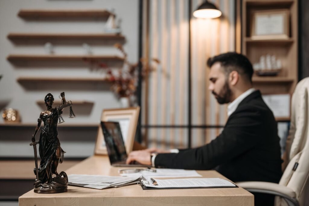 A lawyer works on a laptop at a desk with a Lady Justice statue