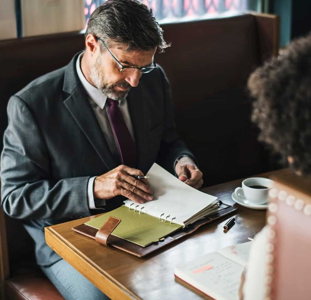 Man in suit reviewing a notebook at a table.