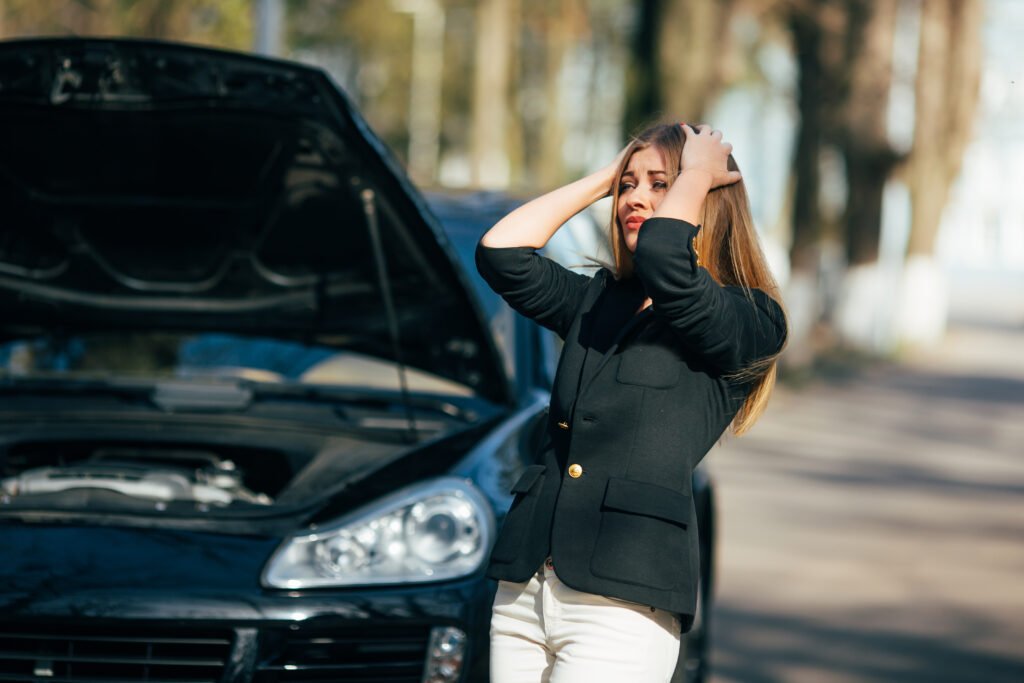 Frustrated woman holding head in front of broken-down car.